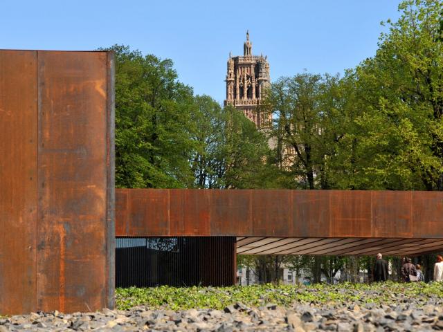 Hall d'entrée du musée Soulages en acier Corten vu de côté avec le clocher de la cathédrale de Rodez en arrière-plan entre les arbres