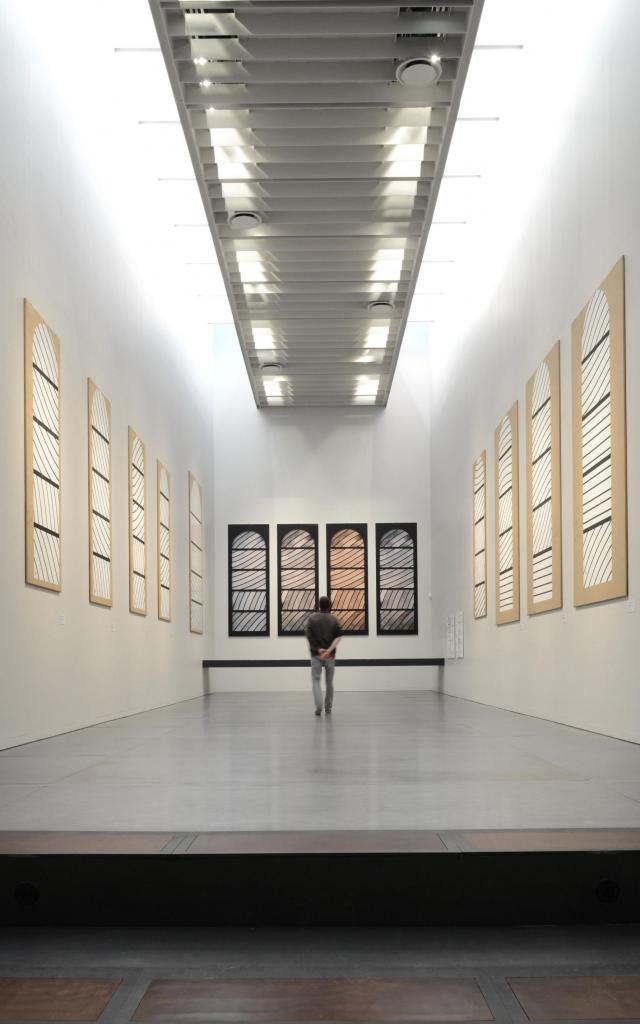 Personne au centre de la Salle de préparation aux vitraux de Conques avec des cartons aux murs et des photos du rendu final selon la luminosité