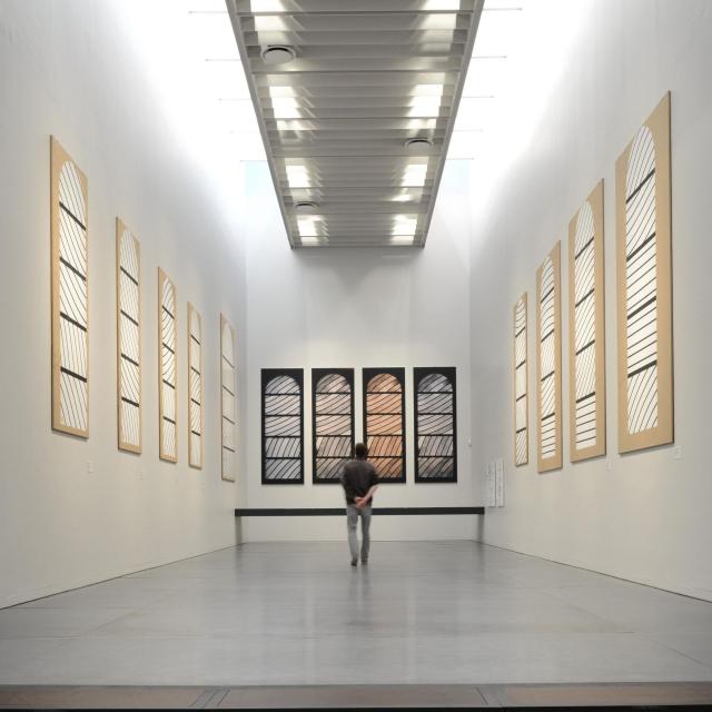 Personne au centre de la Salle de préparation aux vitraux de Conques avec des cartons aux murs et des photos du rendu final selon la luminosité