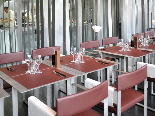 Tables de la salle de restaurant du Café Bras à Rodez, avec la cuisine derrière des stores