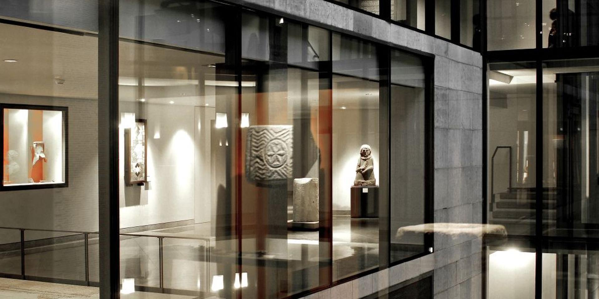 Vue d'une salle du musée Fenaille avec des sculptures, depuis sa cour intérieure