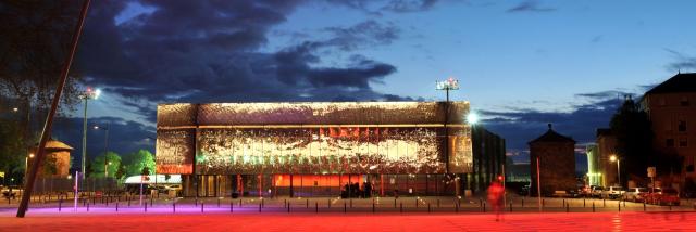 Salle des fêtes de Rodez brillante et son esplanade vues de nuit avec un éclairage rouge contrastant avec la nuit bleue