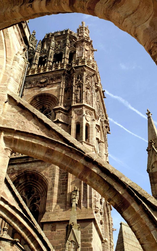 Vue du clocher de la cathédrale de Rodez depuis le toit terrasse, sous une arche avec un ciel bleu