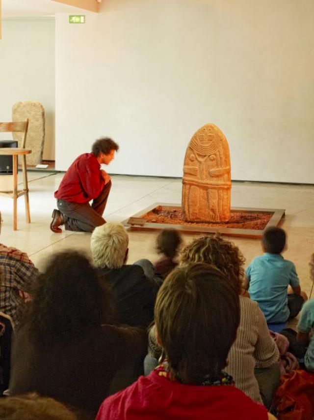 Nombreuses personnes autour d'une statue-menhir, lors d'un atelier au Musée Fenaille de Rodez