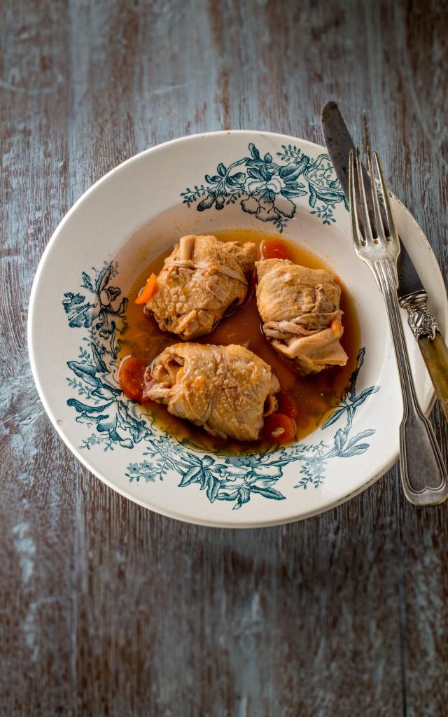Assiettes de trois tripous dans leur sauce avec des carottes, sur une table en bois avec une fourchette et un couteau