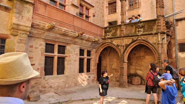 Groupe de personnes en visite guidée au cœur de la maison de Benoit, face au gargouilles et fenêtres à meneaux en grès rouge