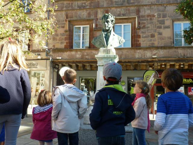 Groupe d'enfants en visite guidée, devant une sculpture sur la place du Bourg