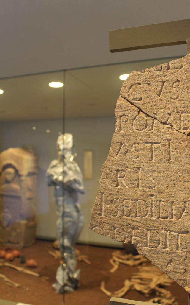 Morceau de pierre gravé avec des écritures, devant une vitrine d'objets archéologiques, au musée Fenaille