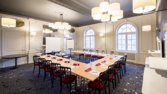 Salle de réunion en forme de U, avec des tables et des chaises en bois pour quinze personnes, dans une salle blanche aux luminaires modernes de l'hôtel Mercure