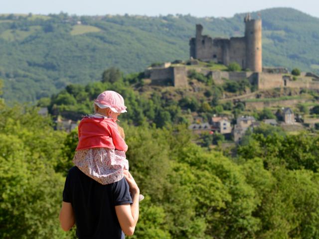 Un homme avec une petite fille sur ses épaules face à la vue sur la forteresse de Najac et la nature environnante