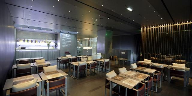 Salle de restaurant du Café Bras avec des fauteuils dotés de coussins blancs, des tables avec des sets, dans un environnement feutré