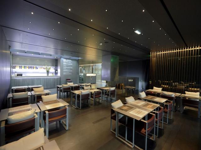 Salle de restaurant du Café Bras avec des fauteuils dotés de coussins blancs, des tables avec des sets, dans un environnement feutré