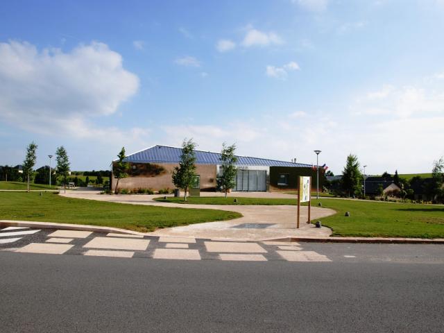 Bâtiment de la mairie de Druelle-Balsac, au bord d'un parc arboré et derrière un panneau signalétique de randonnée