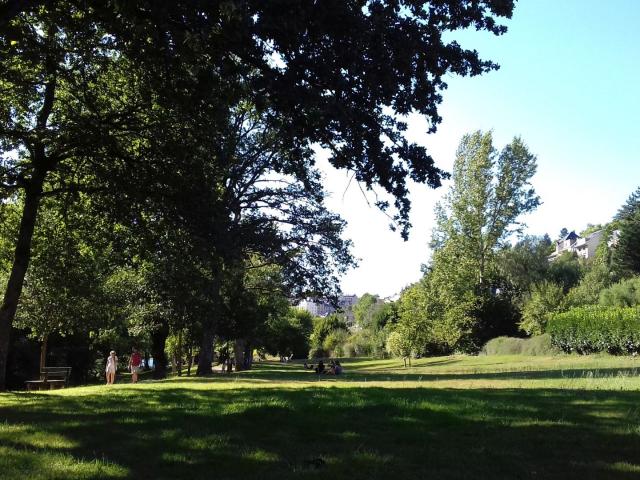 Personne qui se baladent sur le chemin piétonnier au bord de l'espace vert arboré à Layoule où des gens sont assis dans l'herbe