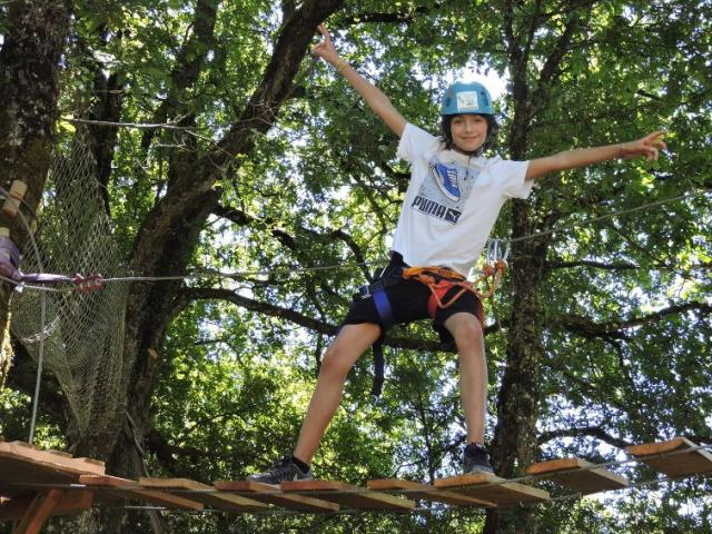 Enfant qui effectue un parcours Accrobranche, accroché via au baudrier à une ligne sécurisée