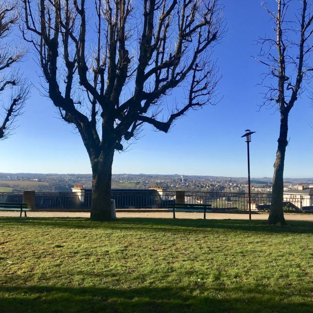 Vue sur Rodez et Olemps depuis le square Fabié où il y a des bancs, une promenade et des arbres nus