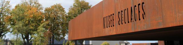 Enseigne du musée Soulages gravée dans l'acier Corten, face à son jardin arboré et son ciel dégagé