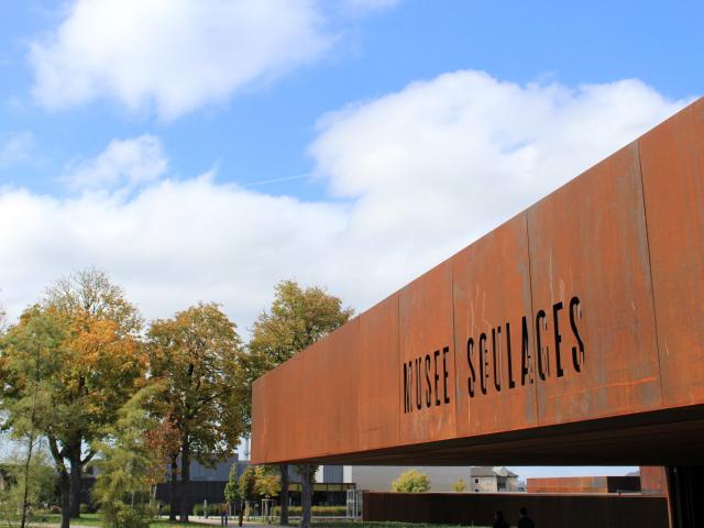 Enseigne du musée Soulages gravée dans l'acier Corten, face à son jardin arboré et son ciel dégagé