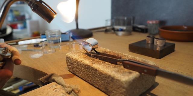Création d'une bague en métal, chauffée au chalumeau, maintenue par une pince sur un bloc de pierre