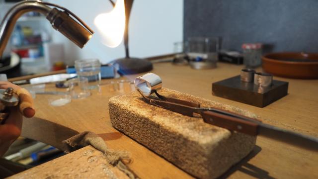 Création d'une bague en métal, chauffée au chalumeau, maintenue par une pince sur un bloc de pierre