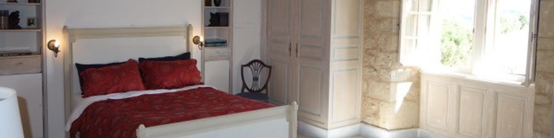 Chambre double du château de Balsac avec un lit au par-dessus rouge, une armoire blanche en bois, et un luminaire style bougies, devant une fenêtre ouverte