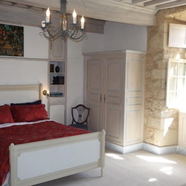 Chambre double du château de Balsac avec un lit au par-dessus rouge, une armoire blanche en bois, et un luminaire style bougies, devant une fenêtre ouverte