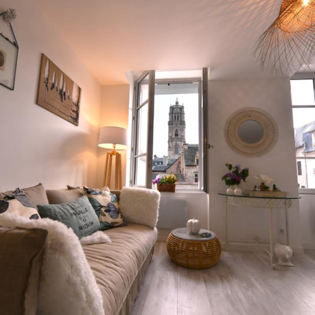 Intérieur cosy du meublé Le Clos de l'Évêché avec son canapé à côté d'une fenêtre ouverte sur la cathédrale