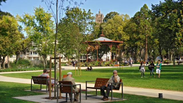 Personnes assises sur des bancs dans le jardin public face au kiosque et au clocher de la cathédrale