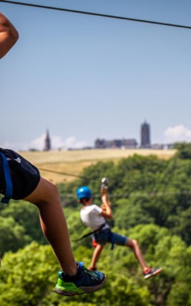 Personnes sur deux tyroliennes parallèles, portant un teeshirt floqué Vert Tea Jeu, avec la cathédrale au loin