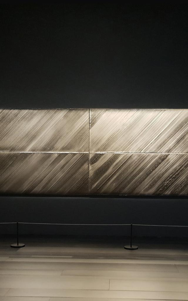 Personne qui admire un tableau horizontal Outrenoir de Pierre Soulages exposé dans une salle du musée