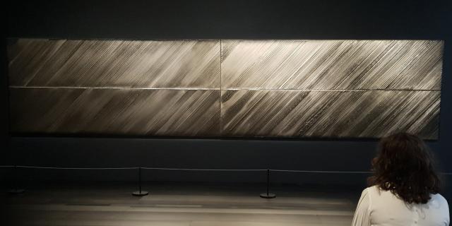 Personne qui admire un tableau horizontal Outrenoir de Pierre Soulages exposé dans une salle du musée