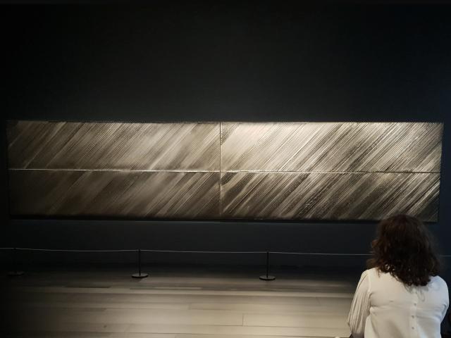 Personne qui admire un tableau horizontal Outrenoir de Pierre Soulages exposé dans une salle du musée