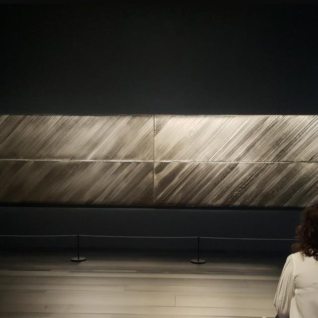 Personne qui admire un tableau horizontal Outrenoir de Pierre Soulages exposé dans une salle du musée
