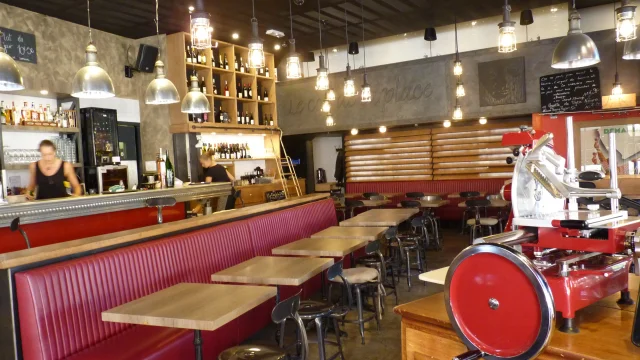 Intérieur du restaurant Le Coq de la Place style bistro avec ses tables en bois le long d'une banquette en cuir rouge et ses chaises en fer
