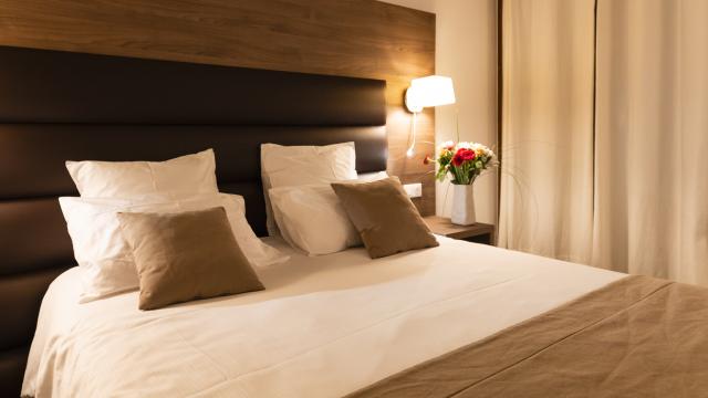 Lit d'hôtel chez Bastide, dans les teintes marron avec un bouquet de fleurs sur la table de nuit au-dessous d'une lampe d'appoint