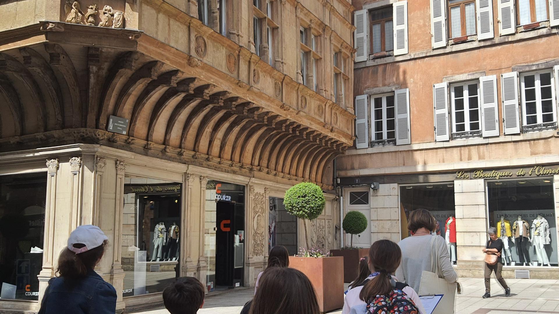 Groupe d'enfants suivant leur guide devant un bâtiment remarquable de Rodez avec des encorbellements : la maison dite d'Armagnac