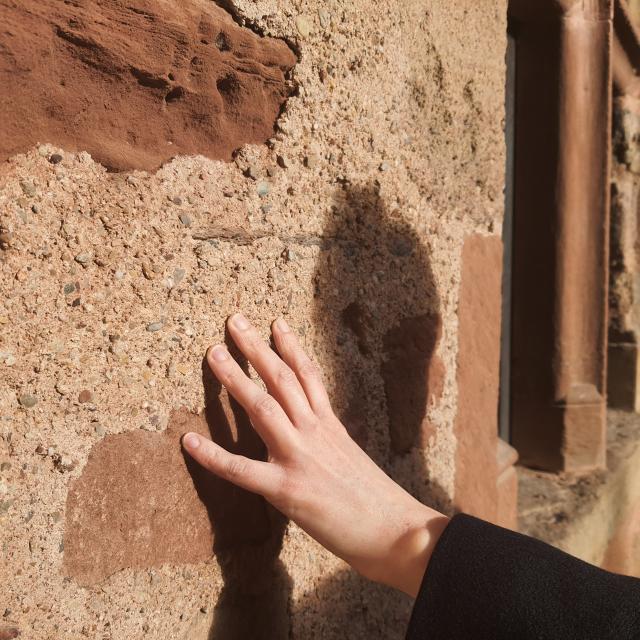 Main effleurant la pierre de grès rose d'un mur