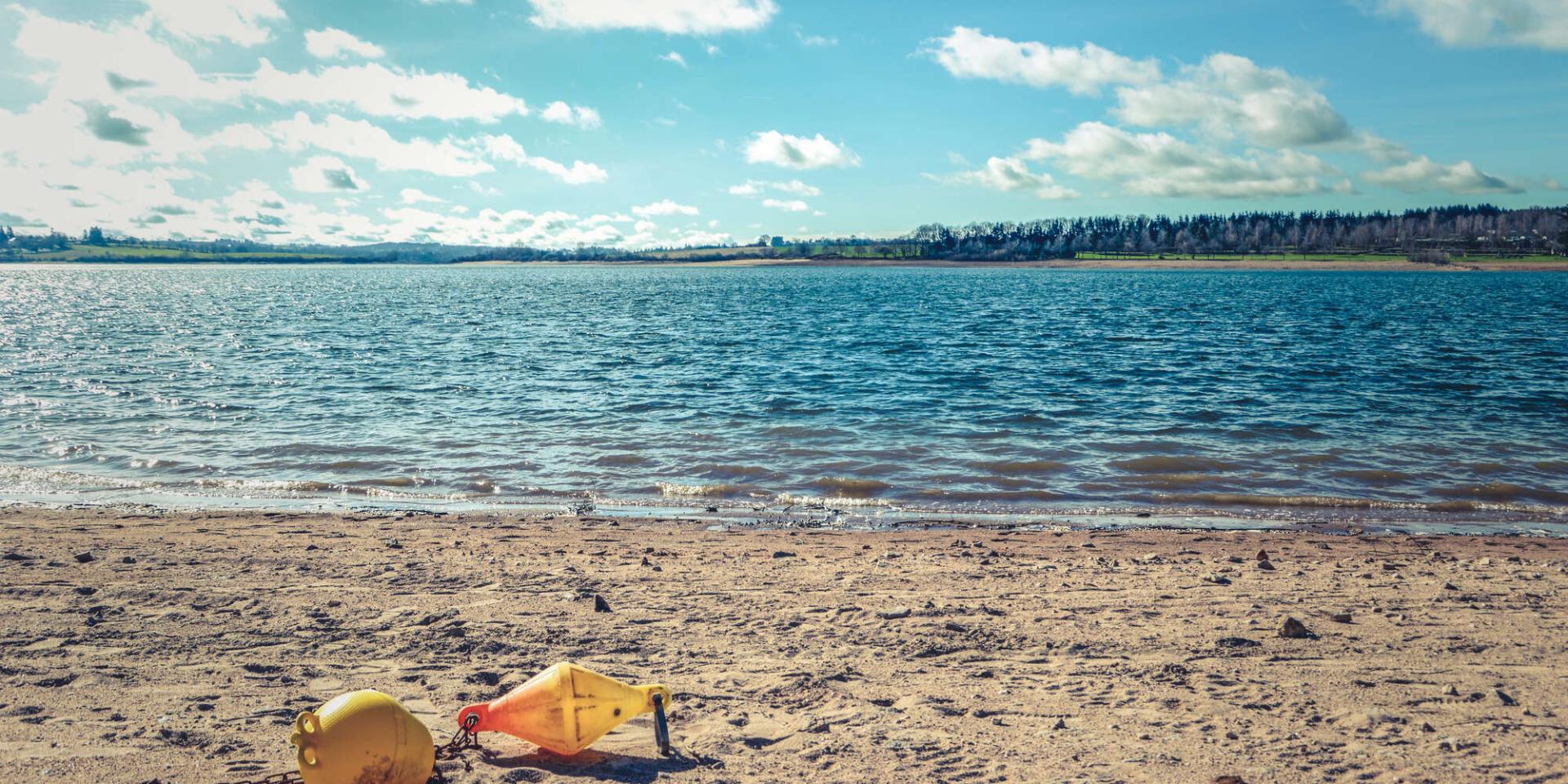 Plage au bord du lac de Pareloup, avec une bouée d'amarrage jaune sur le sable