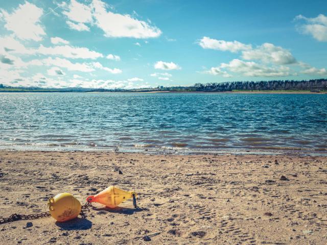 Plage au bord du lac de Pareloup, avec une bouée d'amarrage jaune sur le sable