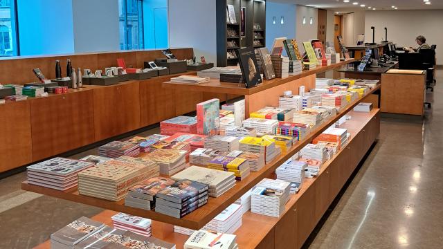 Rayon librairie du musée Fenaille avec des piles d'ouvrage sur un meuble en bois avec trois étagères