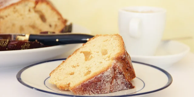 Part de fouace sucrée couchée sur une petite assiette en porcelaine à côté d'une tasse à café