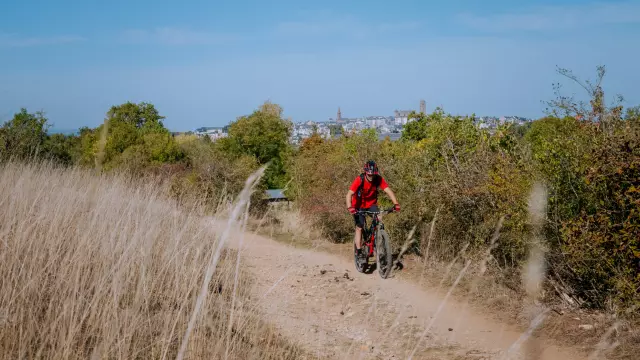 Personne à VTT sur un chemin de terre dos à la cathédrale de Rodez aperçue en hauteur