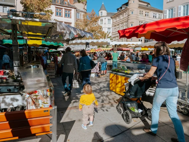 Famille avec poussette et jeune enfant entre les étals du marche de Rodez, devant la foule de chalands